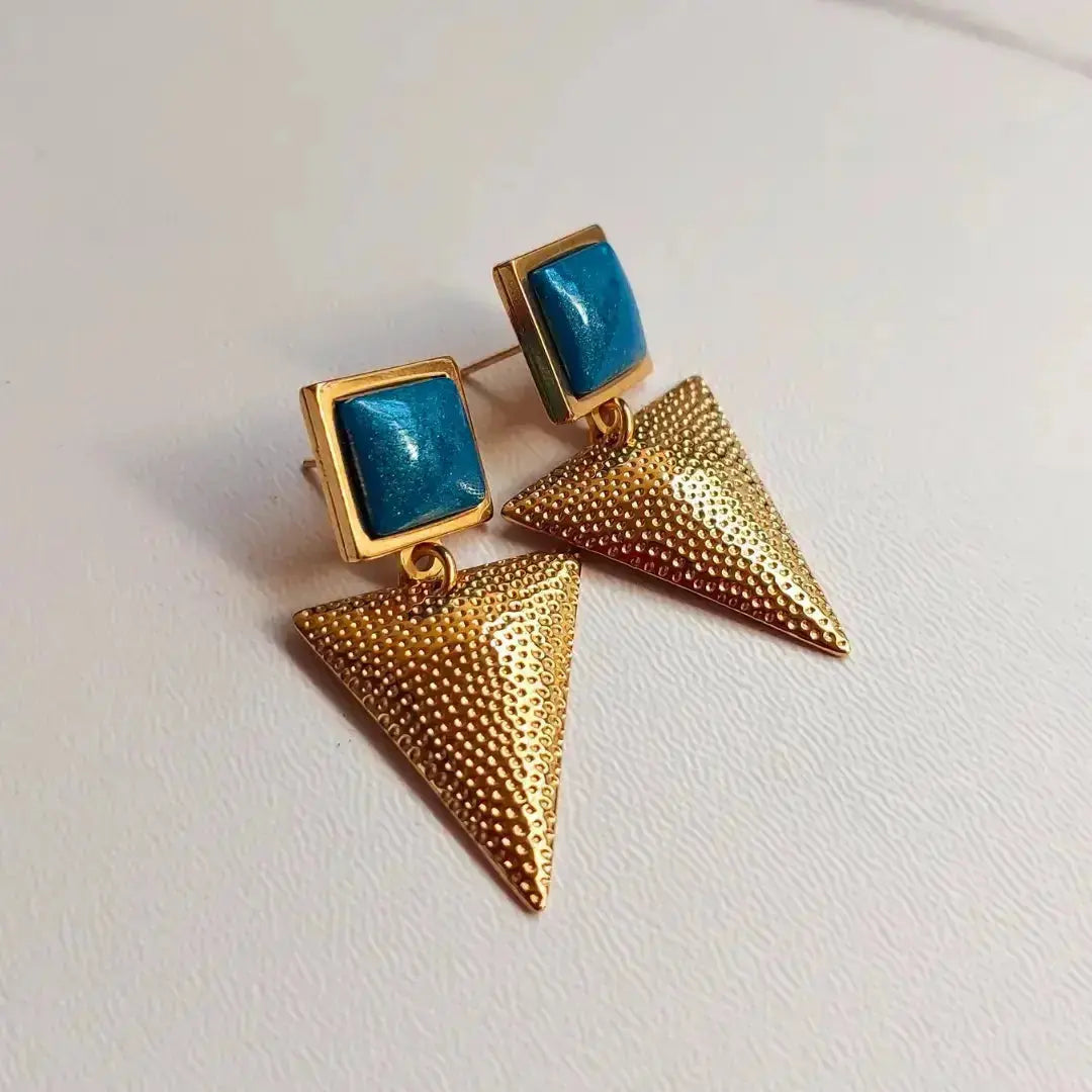 Ručno rađene minđuse u boji zlata sa petrolej kamenom i teksturisanim trouglovima na svetloj pozadini.